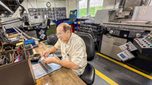 Manufacturing employee seated at a workbench inspecting small machined components inside the Ripley Tools production facility, surrounded by machining equipment and tooling.